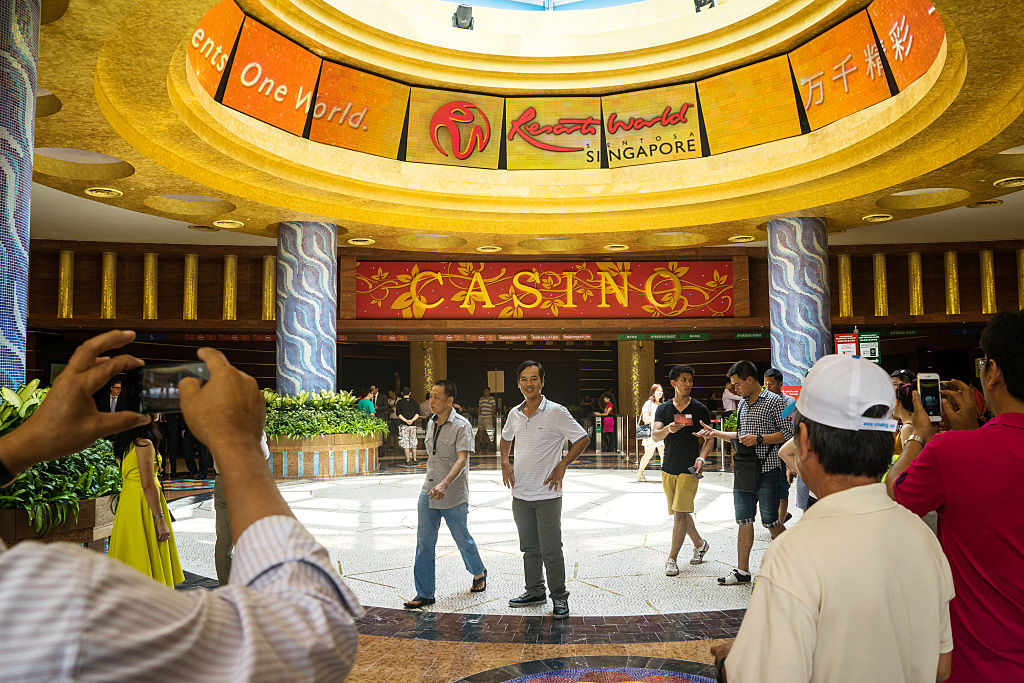 Visitors take photographs in front of the casino at Resorts World Sentosa, operated by Genting Singapore Plc., in Singapore, on Thursday, March 26, 2015. Companies ranging from Singapore Airlines Ltd. to Google Inc. have paid tribute to the late Lee Kuan Yew, Singapore's first prime minister. The city's two casino resorts including Marina Bay Sands canceled their nightly iconic light and water shows. Genting Singapore also halted street acts at its Universal Studios theme park and suspended marketing events. Photographer: Sanjit Das/Bloomberg via Getty Images