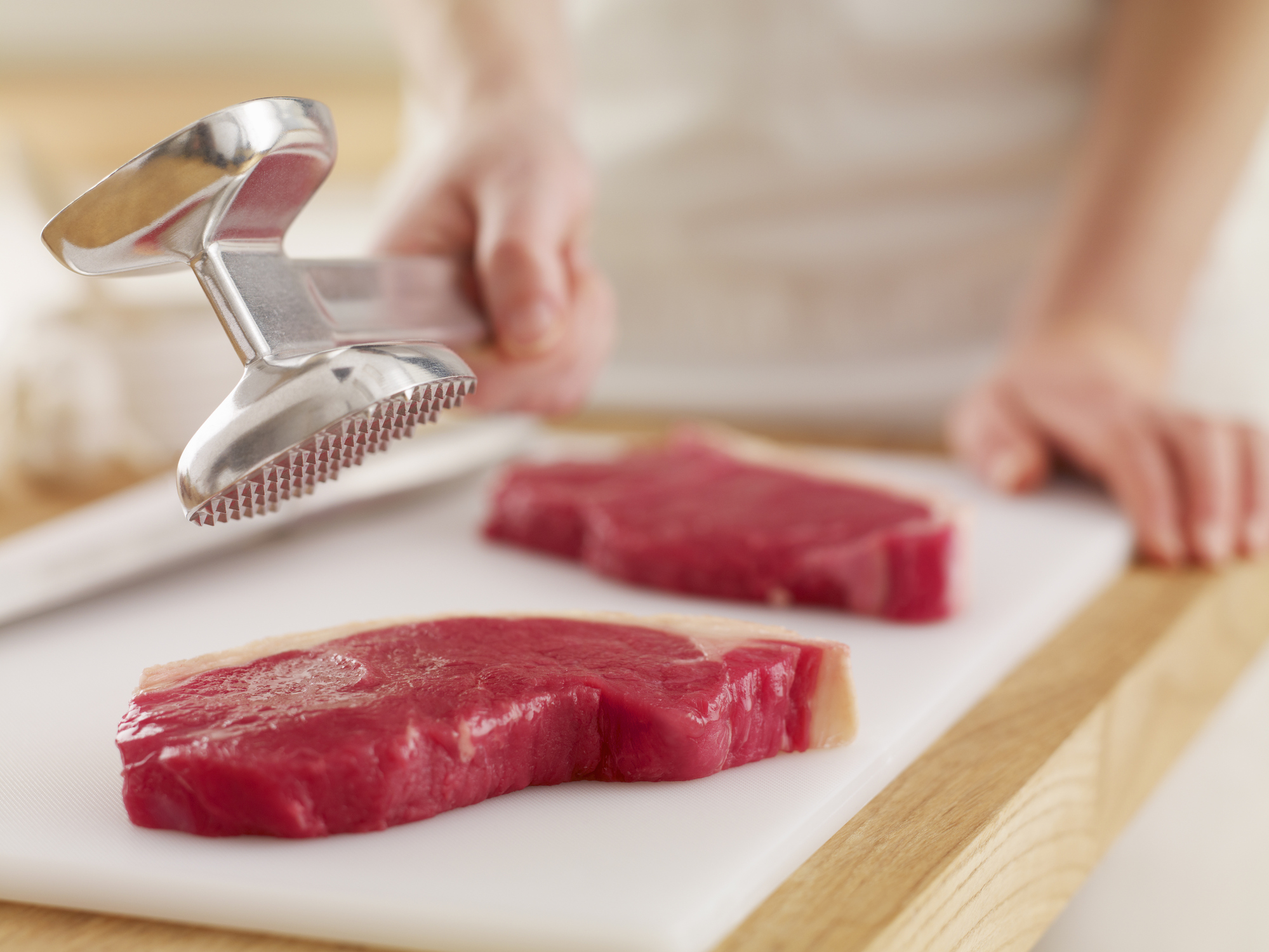Woman holding tenderizer over raw steaks