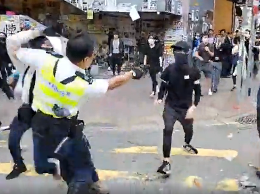 hong kong police officer aiming a gun at a protester advancing toward him
