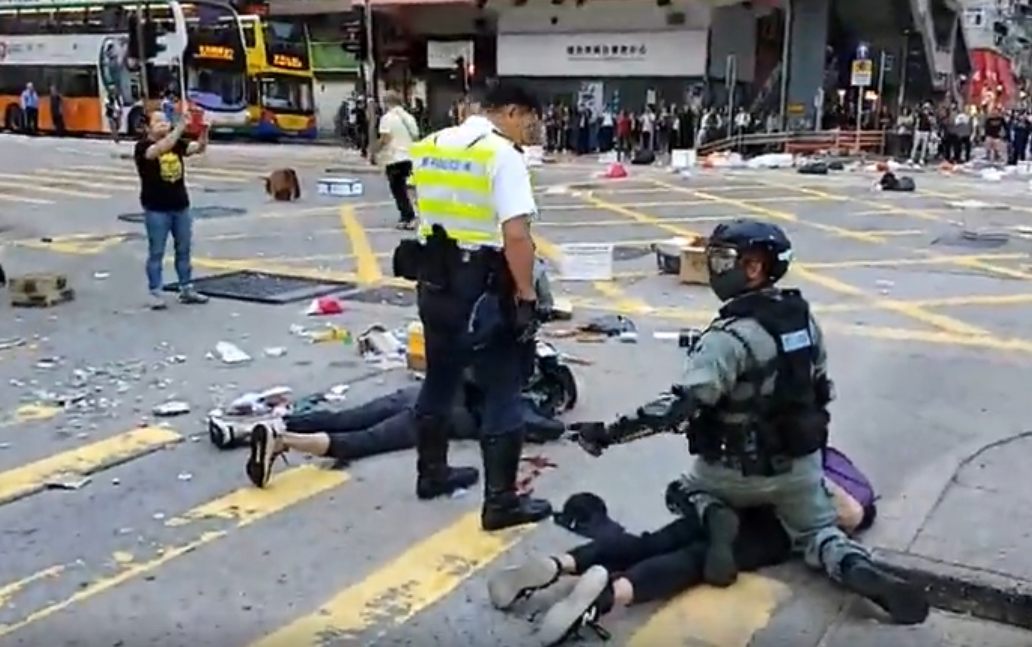 hong kong police officer standing over a protester lying facedown on the ground