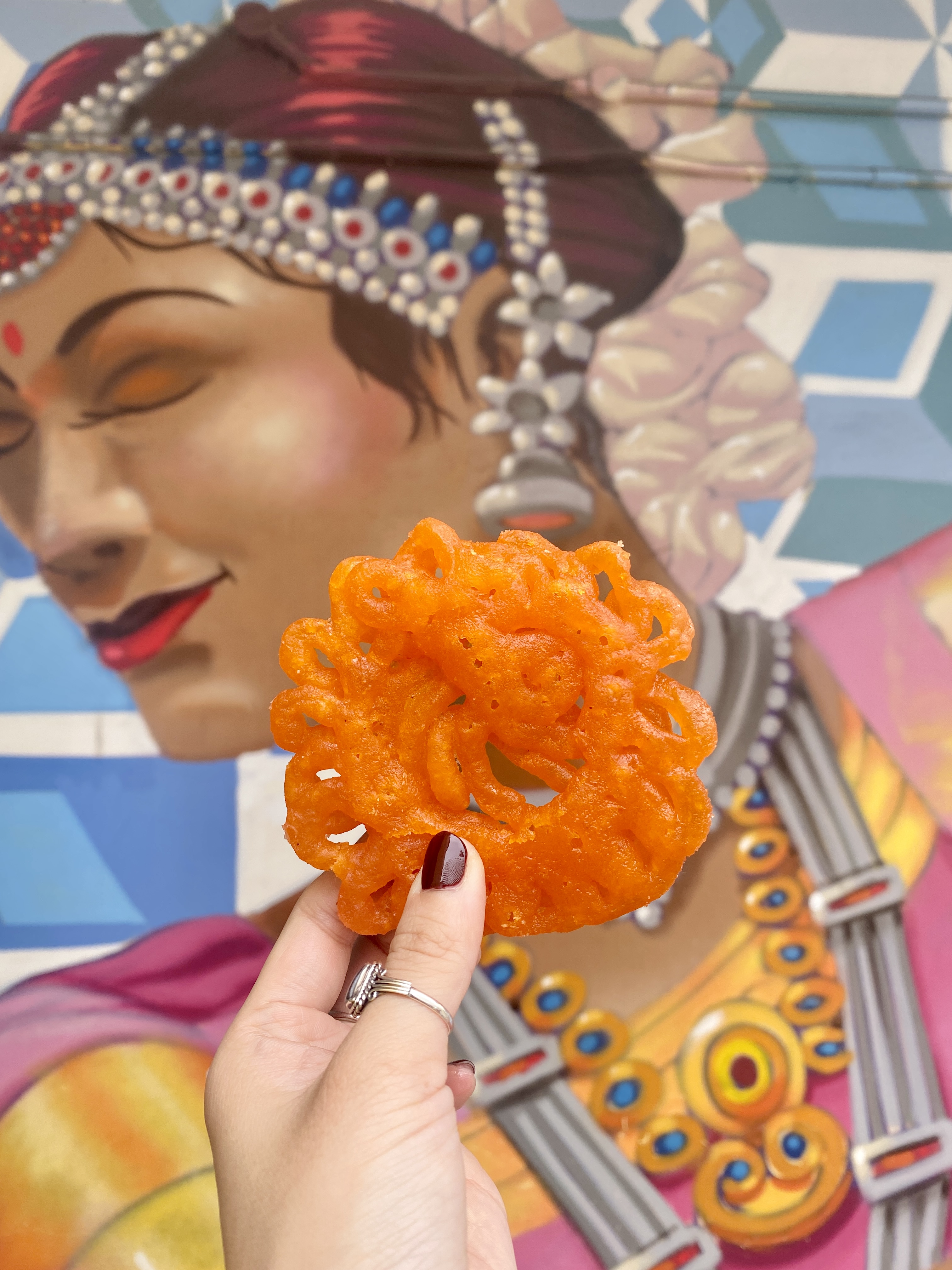 image of an orange indian snack - jalebi against a brightly colored wall