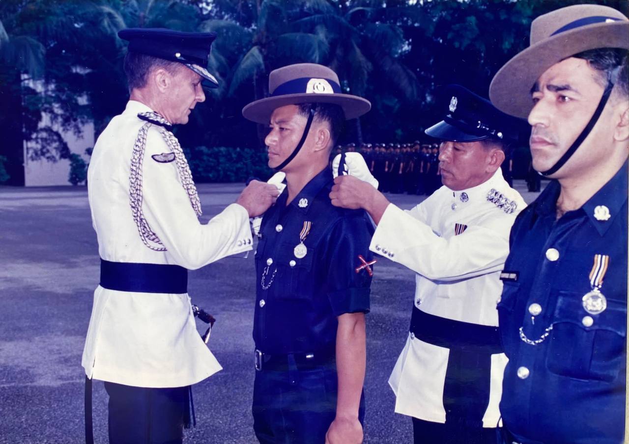 A man dressed in navy blue police uniform is ceremoniously adorned by two officers in white coats.