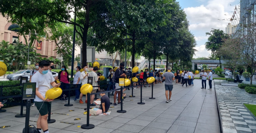 A long queue at on a street lined with trees.