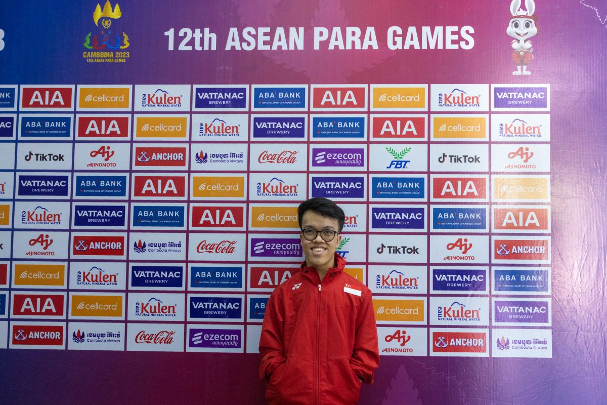 Lim poses in front of a wall that says "12th ASEAN PARA GAMES," dressed in a red Team Singapore suit.