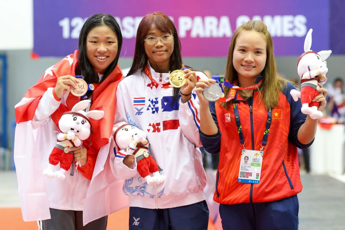 Tong stands on the left, holding a bronze medal. Kangpila stands in the middle, holding a gold medal. Hồ stands on the right, holding a silver medal. All three athletes pose for the camera, smiling, and holding a rabbit plush toy.