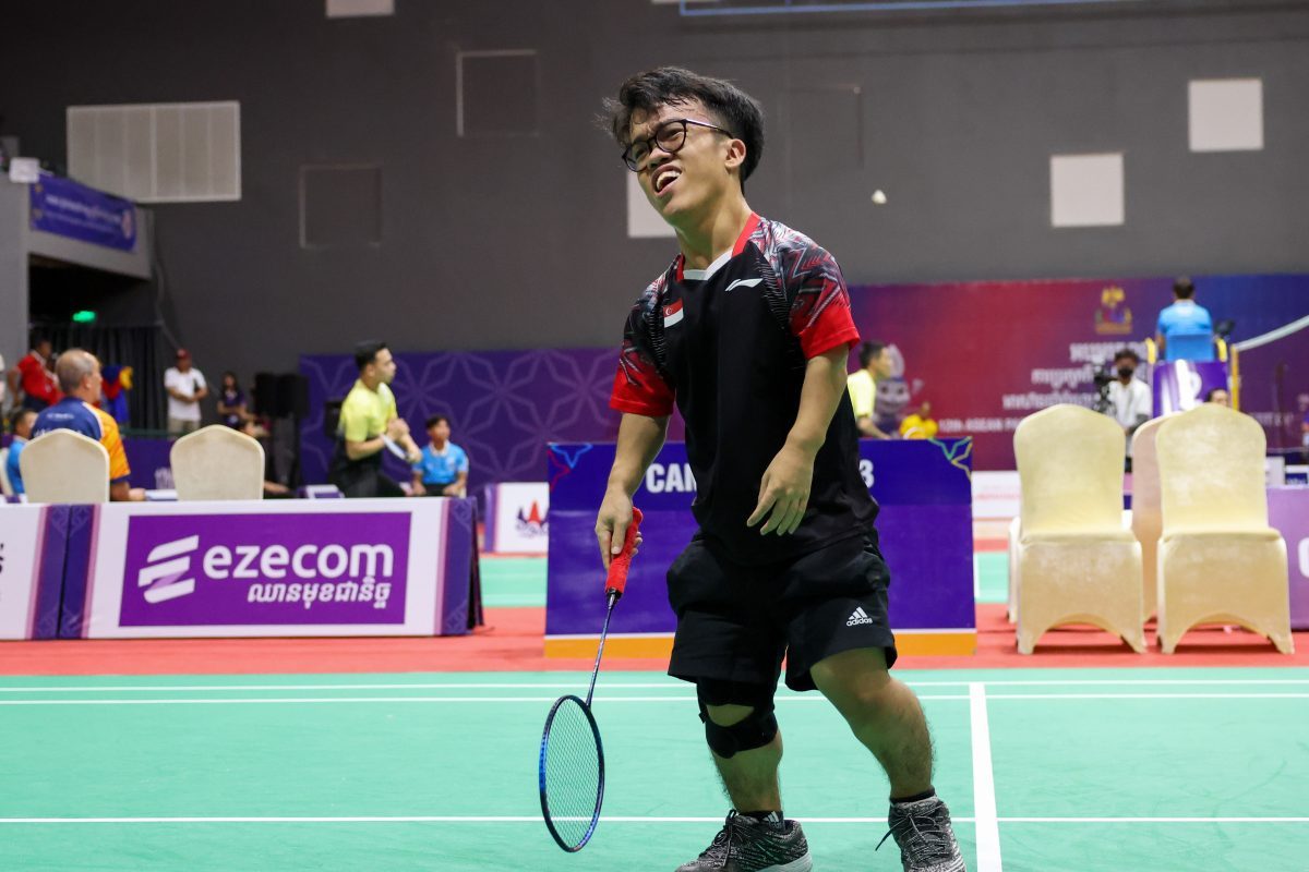 Lim is dressed in a black t-shirt, holding a racket and looking disappointed.