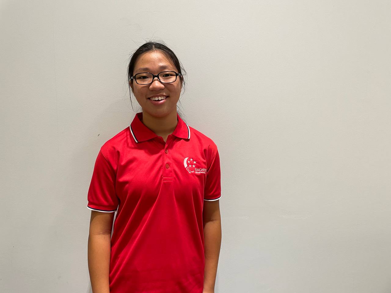 Tong smiles for the camera, dressed in a red polo t-shirt and standing in front of a white background.