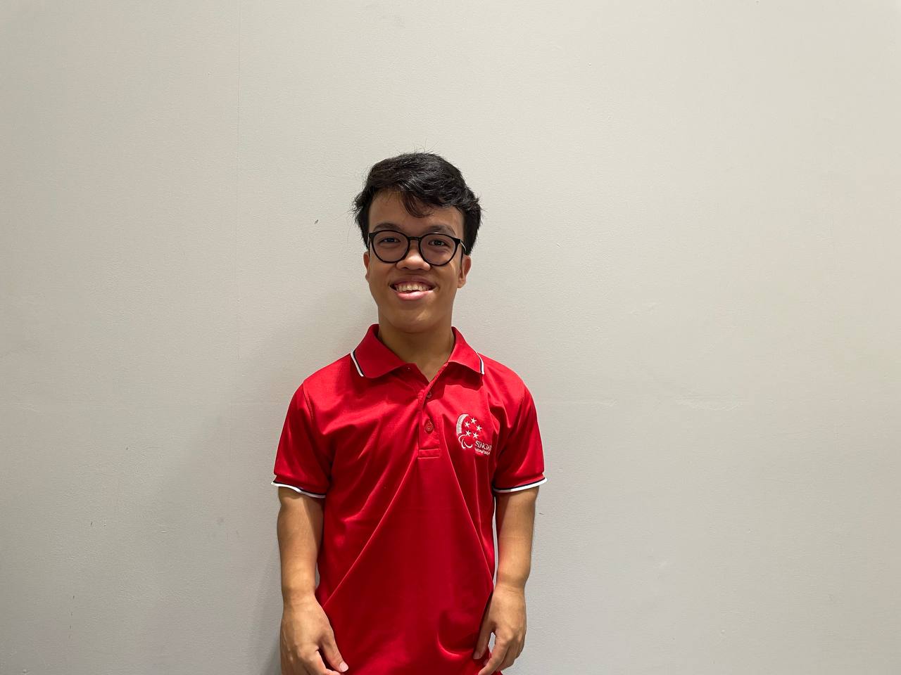 Lim smiles for the camera, dressed in a red polo t-shirt and standing in front of a white background.