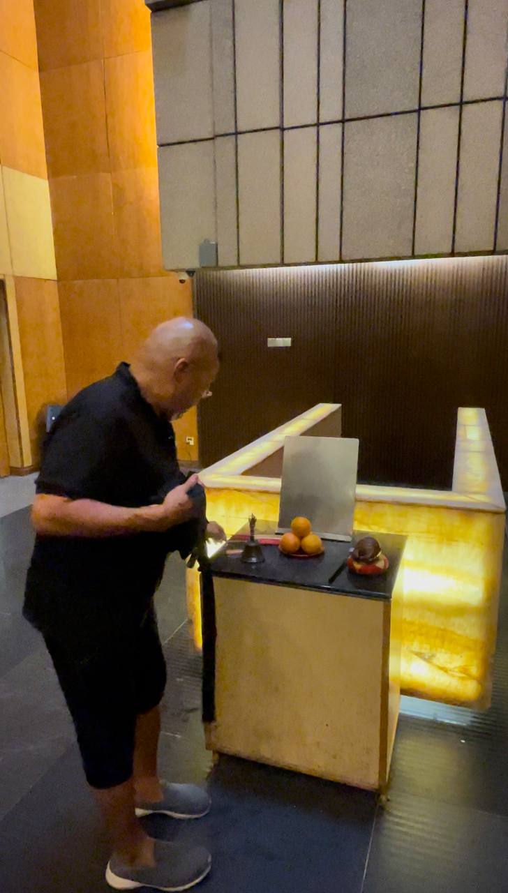 Yu, dressed in a black shirt, prepares for the last rites of an estranged, dead person. There are unlit candles and mandarins placed on the table in front of him.