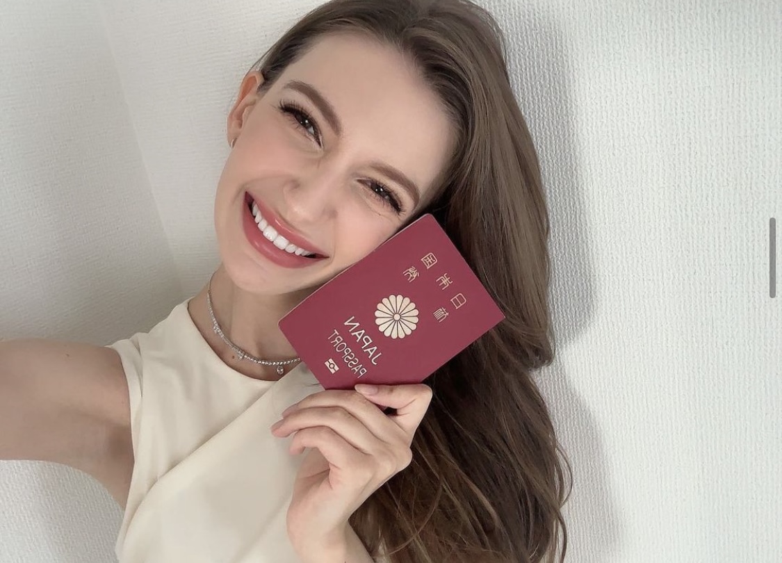 Image of Shiino, smiling, holding a Japanese passport.
